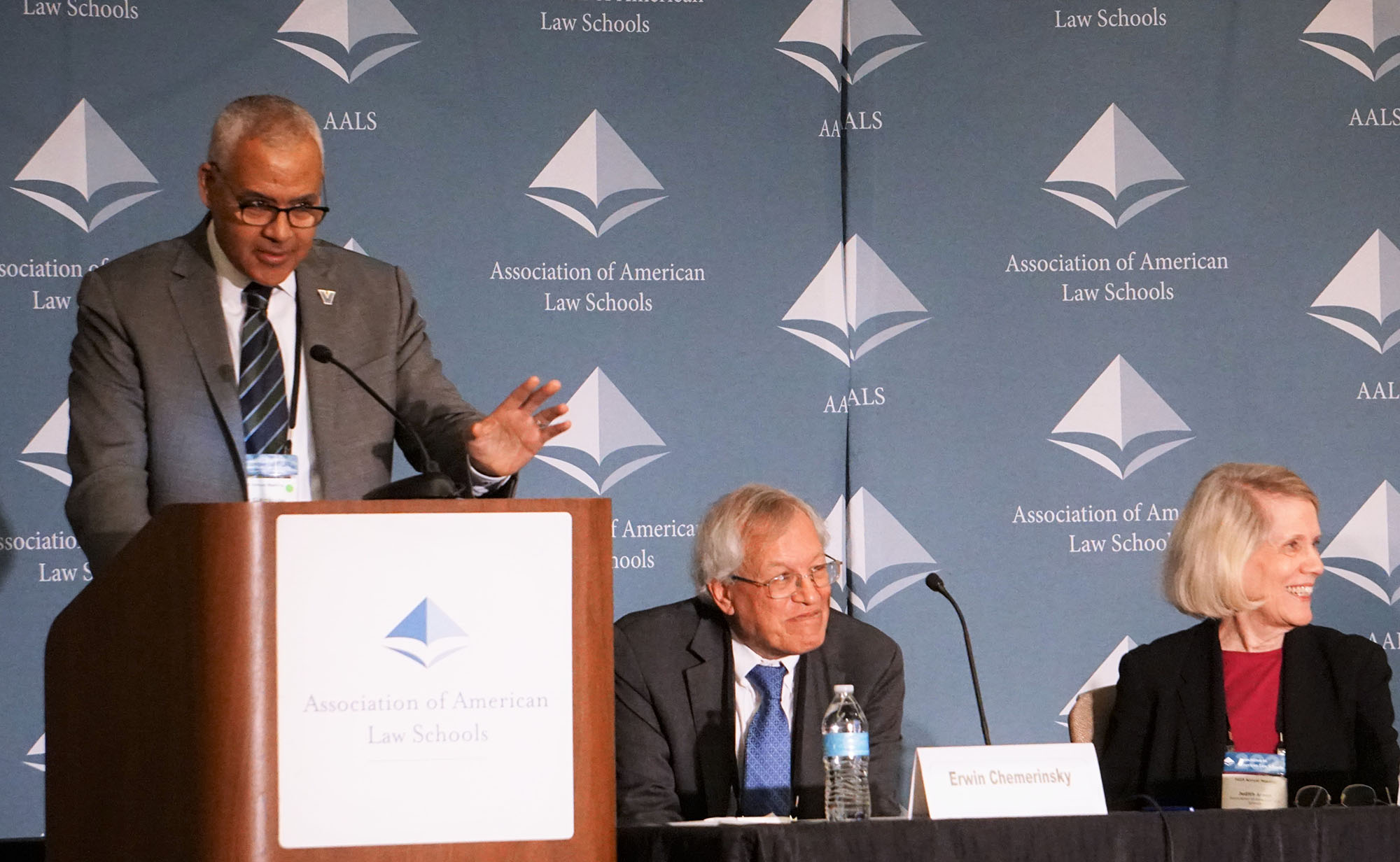 Mark C Alexander standing at a podium with Erwin Chemerinsky and Judy Areen on a table behind him