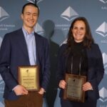 Two smiling people holding their plaques at a conference